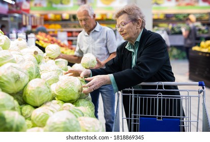 reife Kaukasierin mit Brille wählt einen Kopf Kohl im Gemüsebereich des Supermarkts aus