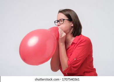 Mature Caucasian Woman In Glasses Tyring To Blow Red Balloon Testing Her Breathing System. Studio Shot