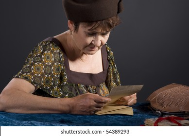 Mature Caucasian Woman Reading Old Letter. Studio Photo On Grey Background