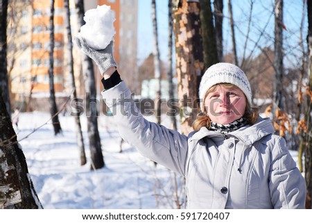 Mature caucasian woman in the snowy park with a snowball