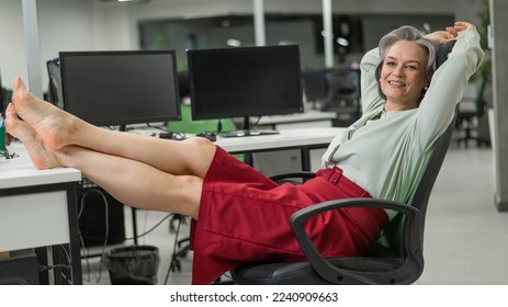 Mature caucasian woman took off her shoes and put her feet on the desktop in the office.  - Powered by Shutterstock