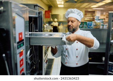 Mature chef using professional oven while preparing food in a restaurant. 