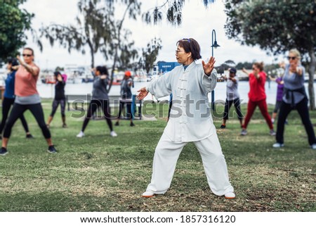 Mature chinese woman do tai chi with blirred group of people outdoor in the park