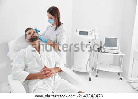 Mature client sits in armchair while cosmetologist does meso therapy procedure in beauty salon
