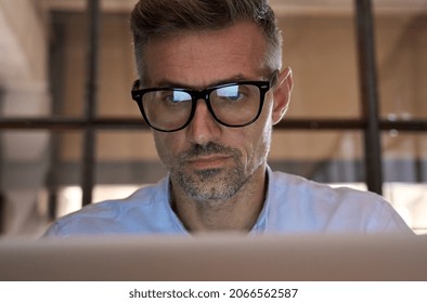 Mature concentrated business man trader wearing eyeglasses working looking at laptop computer screen reflecting in glasses analyzing online trading market financial digital data graph. Close up view