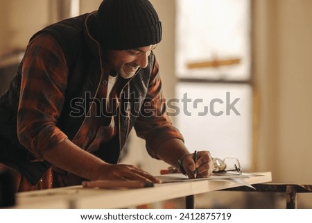 Mature contractor happily works on renovating a kitchen interior, drawing on blueprints with a pencil. Skilled in construction and refurbishment, he showcases expertise in home remodeling.