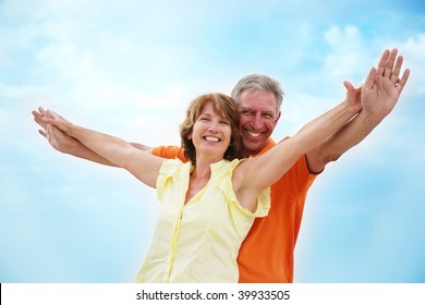 Mature couple with arms outstretched over a blue sky background - Powered by Shutterstock