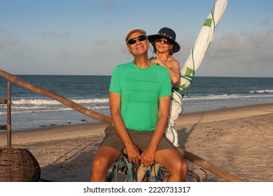 Mature Couple At The Beach In Combuco, Brazil, Sitting On A Jangada A Fishing Boat Typical In Brazil