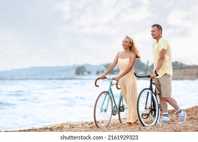 Mature couple with bicycles walking along sea beach on summer day - Powered by Shutterstock