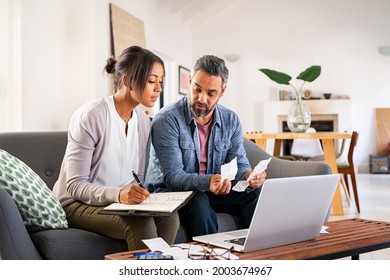 Mature couple calculating bills at home using laptop. Multiethnic couple working on computer while calculating finances. Mature indian man with african american woman at home analyzing their finance.