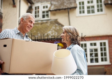 Mature Couple Carrying Boxes On Moving Day In Front Of Dream Home