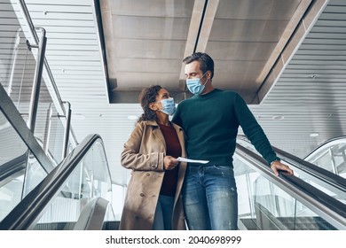 Mature Couple Carrying Tickets While Moving By Escalator In Airport Terminal