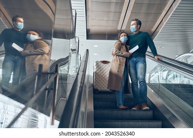 Mature Couple Carrying Tickets While Moving By Escalator In Airport Terminal