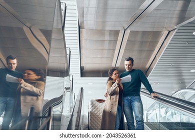 Mature Couple Carrying Tickets While Moving By Escalator In Airport Terminal