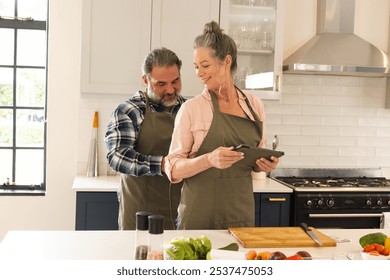 Mature couple cooking together in kitchen, using tablet for recipe inspiration, at home. technology, lifestyle, home, culinary, healthy eating - Powered by Shutterstock