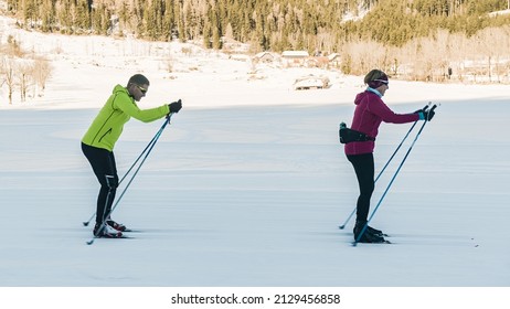 Mature couple cross country skiing one behind the other, making coordinated body and ski poles movements.