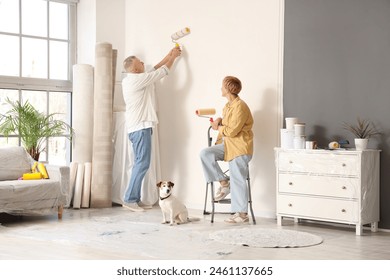 Mature couple with dog painting wall during repair in their new house - Powered by Shutterstock