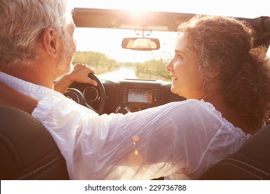 Mature Couple Driving Along Country Road In Open Top Car