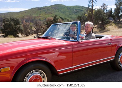 Mature Couple Driving Classic Red Convertible Car On Road Trip