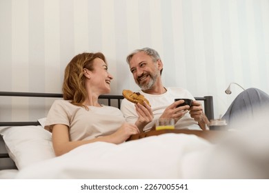 Mature couple enjoying coffee and breakfast in bed - Powered by Shutterstock