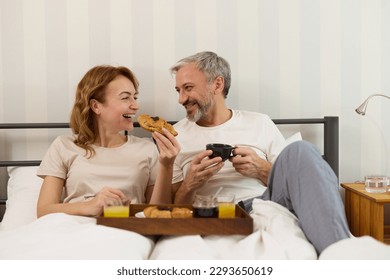 Mature couple enjoying coffee and breakfast at home
in bed - Powered by Shutterstock