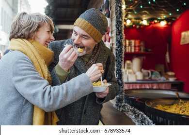 Mature couple are enjoying sharing some paella from a christmas market stall