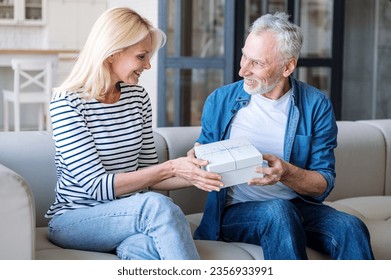 Mature couple exchanging gifts, expressing love. Spouses celebrating special occasion at home, spending romantic weekend together. Man congratulating woman. Making joy to partner - Powered by Shutterstock