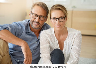 Mature Couple With Eyeglasses Sitting On Carpet At Home