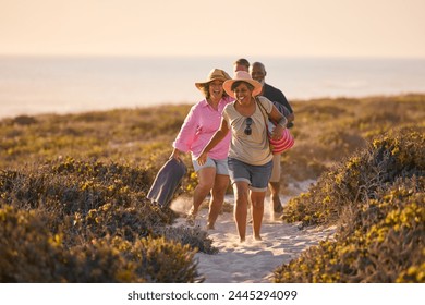 Mature Couple With Friends On Summer Vacation Walking Through Dunes On Way To Beach Carrying Bags - Powered by Shutterstock