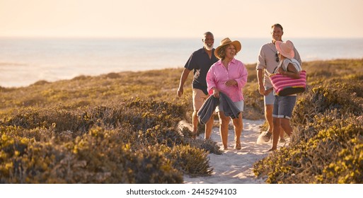 Mature Couple With Friends On Summer Vacation Walking Through Dunes On Way To Beach Carrying Bags - Powered by Shutterstock