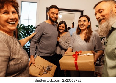 A mature couple greets their smiling guests at home. Laughing adult children came to their parents with gifts. Happy people spend family holidays together. Modern cozy home interior. - Powered by Shutterstock