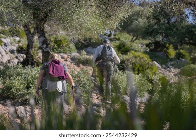 mature couple hiking through mediterranean olive grove in nature landscape. Caucasian couple trekking in mountains with backpacks, hiking clothes and walking stick with copyspace - Powered by Shutterstock