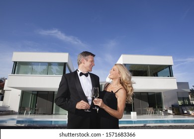 Mature Couple Holding Glasses Of Champagne In Front Of Modern Luxury Home