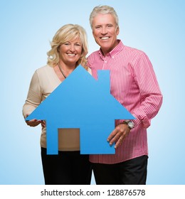Mature Couple Holding Model Of A House against a blue background