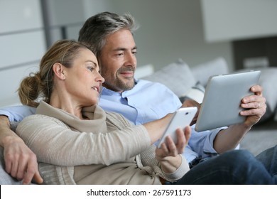 Mature couple at home using smartphone and tablet