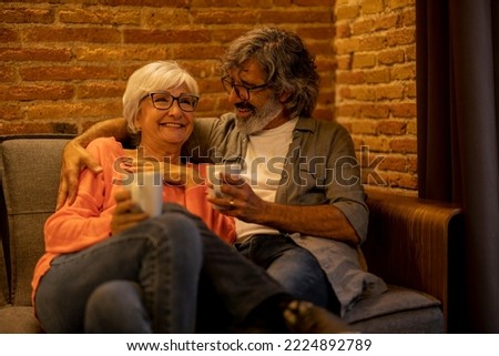 Mature couple with hugging and laughing having a hot drink in a sofa