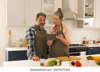 Mature couple in kitchen using tablet for cooking recipe, smiling and engaged, at home. lifestyle, technology, togetherness, engagement, culinary - Powered by Shutterstock