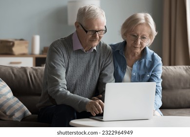 Mature couple learn app, decide purchase through on-line web store look at laptop, reading received e-mail from bank, spend time on internet seated on sofa at home. Baby-boomer spouses and modern tech - Powered by Shutterstock