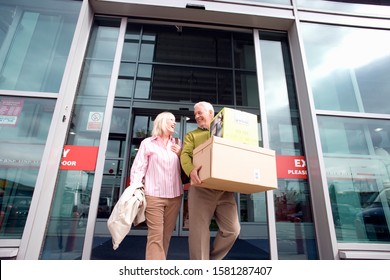 Mature Couple Leaving Electrical Store Carrying Purchases In Boxes