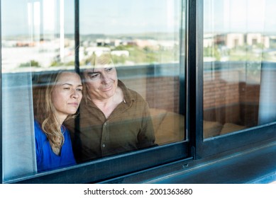 Mature Couple Looking Sad Out The Window From Home.