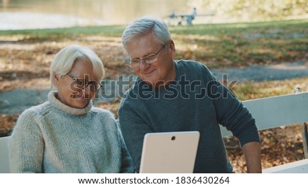 Mature couple in love taking selfie in forest on autumn day. Video call or browsing old photos. High quality photo