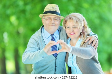 Mature Couple Making A Heart Shape With Their Hands In A Park