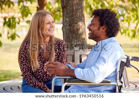 Mature Couple With Man Sitting In Wheelchair Talking In Park Together