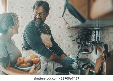 Mature couple man and woman doing housework together with happiness and enjoying life married or in relationship. Man washing dishes in the kitchen and woman holding fruit basket. Real house and life - Powered by Shutterstock