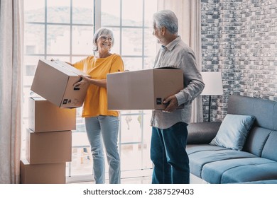 Mature couple moving into new apartment, carrying cardboard boxes into empty room with potted plants. Real estate property buying, relocation, new home concept. Rear view - Powered by Shutterstock