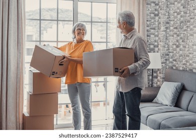 Mature couple moving into new apartment, carrying cardboard boxes into empty room with potted plants. Real estate property buying, relocation, new home concept. Rear view - Powered by Shutterstock