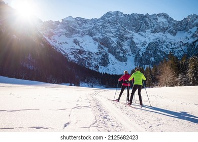 Mature Couple Moving In Sync While Cross Country Skiing On The Ski Trail Surrounded By Mountains And Forest.