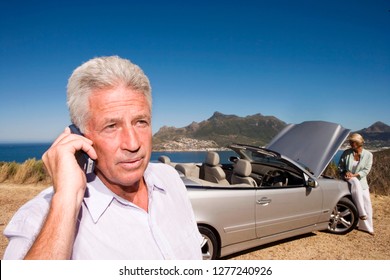 Mature couple on coastal road trip with car breakdown on mobile phone - Powered by Shutterstock