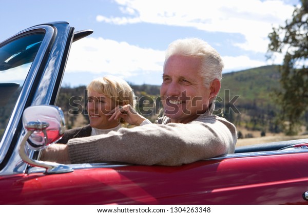 Mature couple on road trip in classic convertible\
car on country road