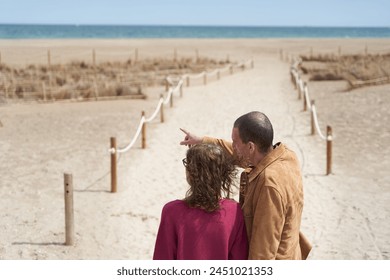 Mature couple in path to the beach pointing at sea - Powered by Shutterstock